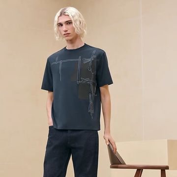 Young man with blonde hair wearing a dark graphic t-shirt and black pants.