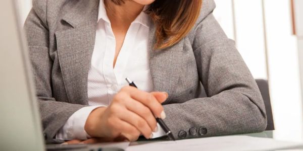 Businesswoman in gray suit writing with a pen at her desk.