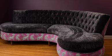 Curved velvet sofa with dark upholstery and pink patterned base.