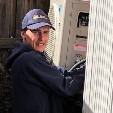 Technician working on an outdoor unit beside a brick house.