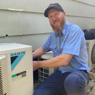 A smiling technician repairing an outdoor air conditioning unit.