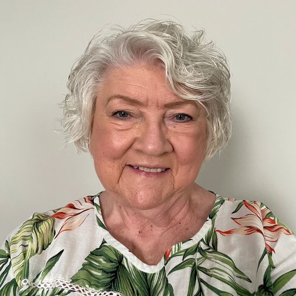 Smiling elderly woman with curly white hair and a floral top.