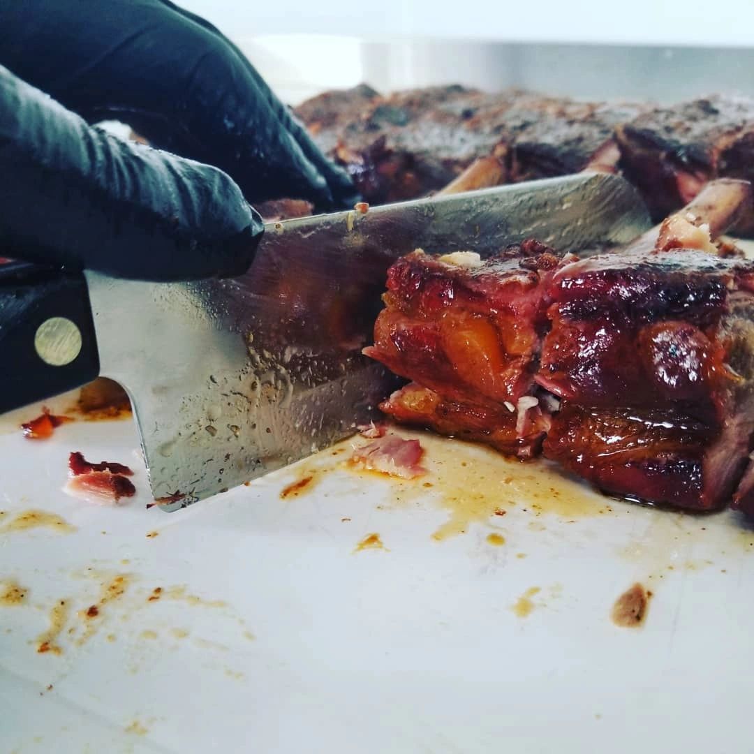 a cleaver cutting into barbecued ribs on a cutting board