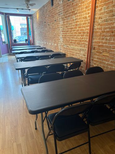 Empty room with black tables and chairs against a brick wall.