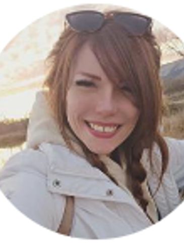 Smiling woman with braided hair outdoors in a white coat and sunglasses on her head.