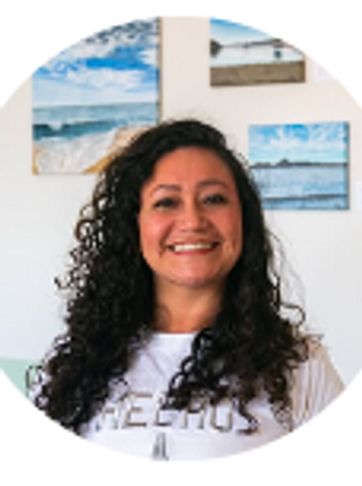 Smiling woman with curly hair in front of beach-themed artwork.