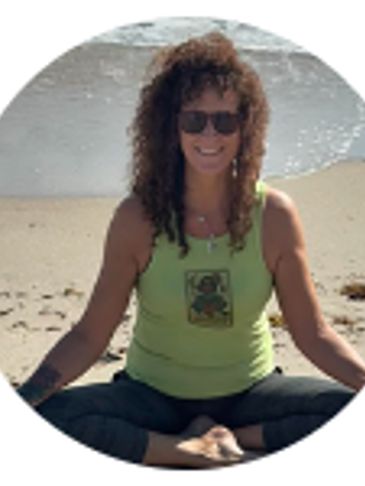 Woman in sunglasses meditating cross-legged on the beach.