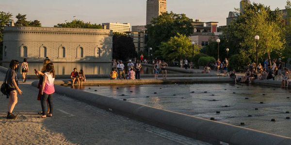 People relax and socialize by a large urban water feature at sunset.