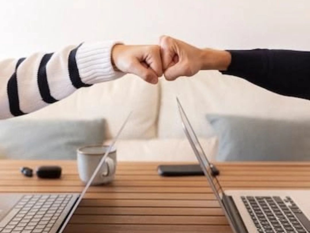 Duas pessoas dando um toque de punho sobre uma mesa com laptops.