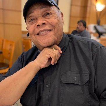 Smiling elderly man resting his chin on his hand indoors.