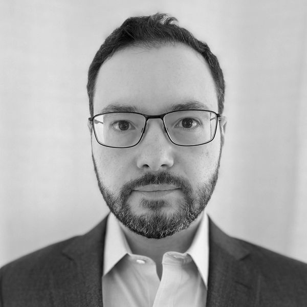 Serious man with glasses and beard in a suit.
