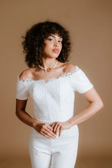 Classic bridal jumpsuit with off the shoulder neckline and short sleeves, trimmed in delicate lace.