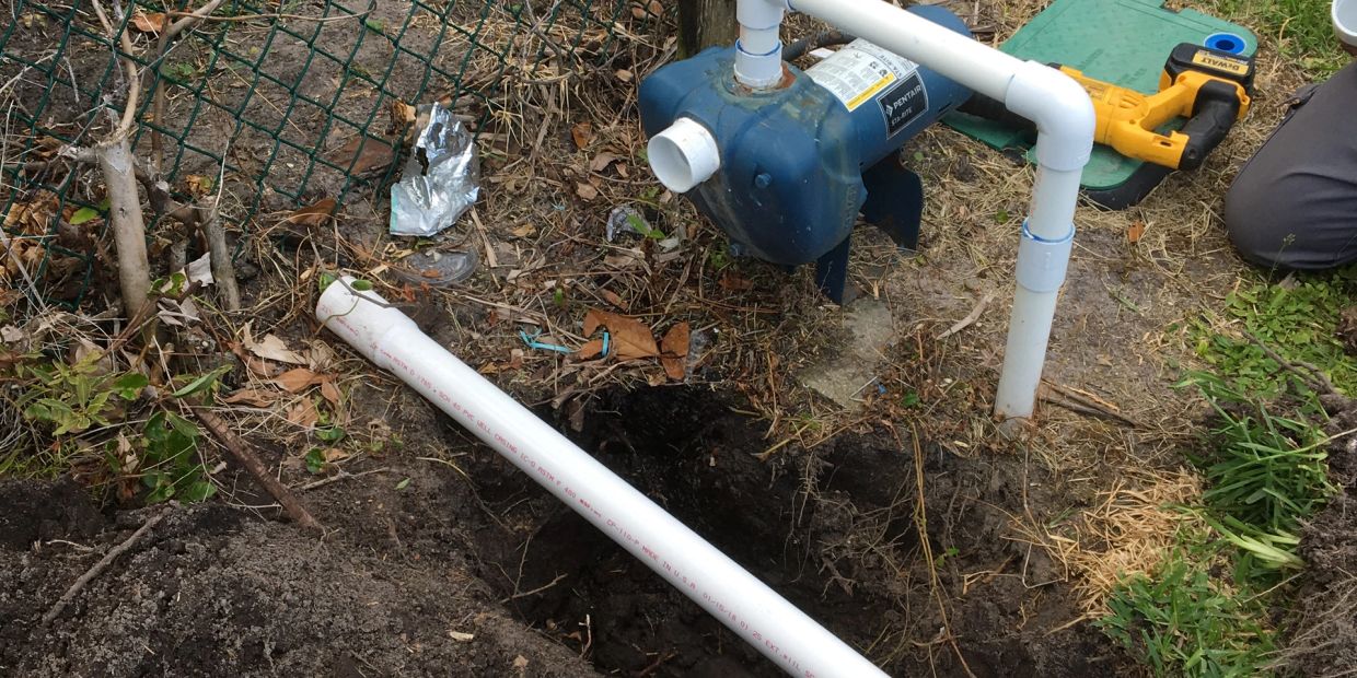 Person working on installing a water pump with PVC pipes.