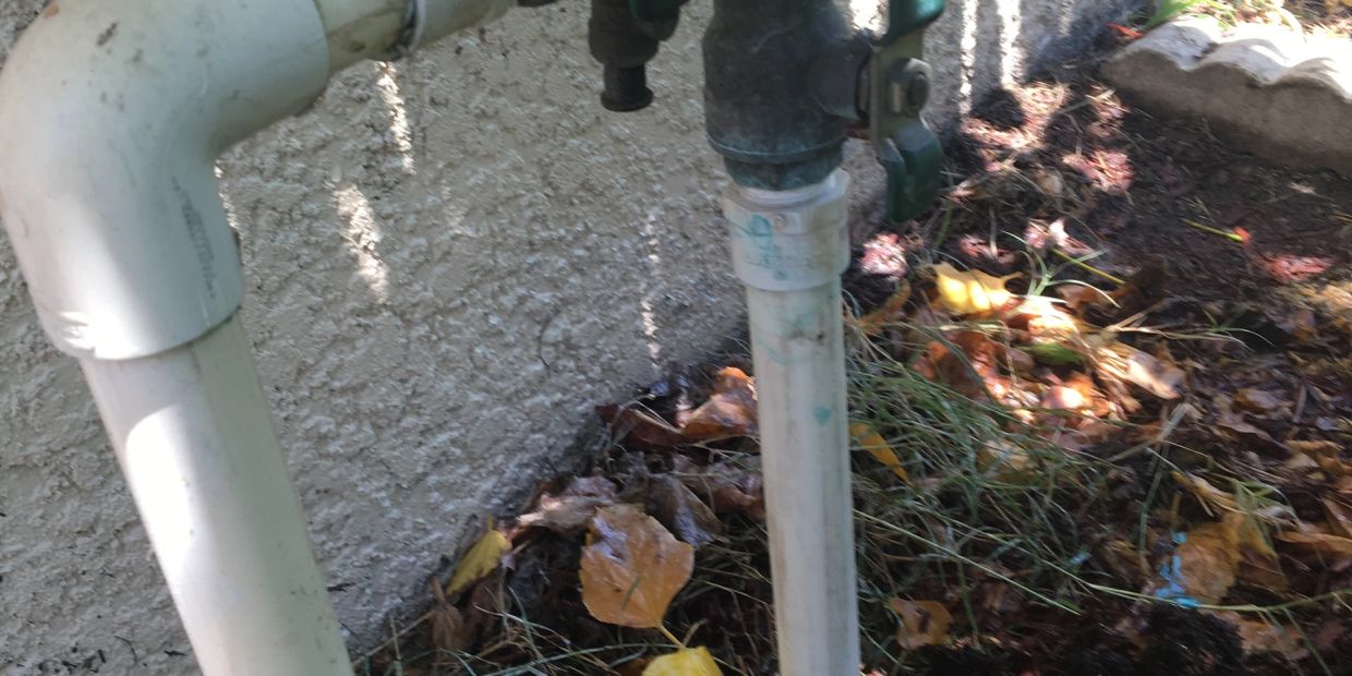 Outdoor water faucet with PVC pipes near a wall.