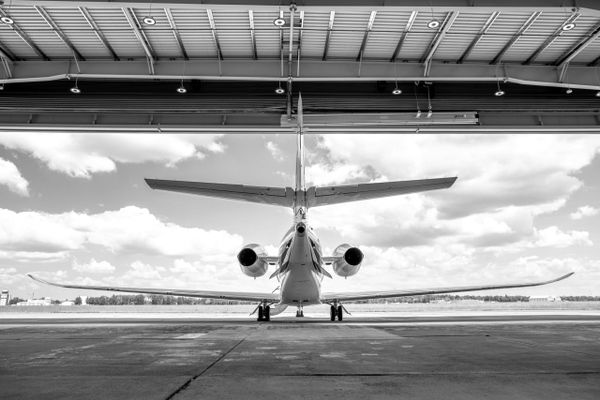 Rear view of an airplane parked inside a hangar under a partly cloudy sky.