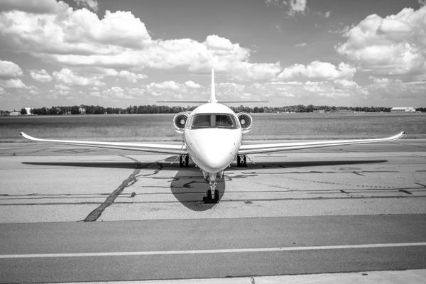Front view of a private jet on a runway under a cloudy sky.