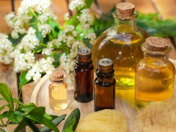 5 glass bottles of aromatherapy oil in a wooden plate and 2 sponges and flowers