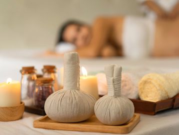 A candle, massage pouches and towels with a pregnant lady getting a massage
