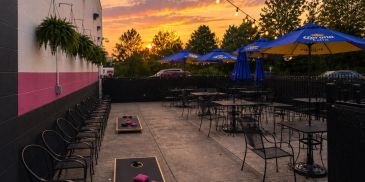 Outdoor patio at That Place Bar & Grill at sunset with tables, umbrellas, string lights, and cornhol