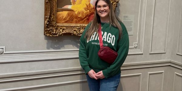 A woman standing and smiling in a museum beside a framed painting.