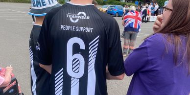 Person wearing a black shirt labeled 'People Support' with the number 6 at an outdoor event.