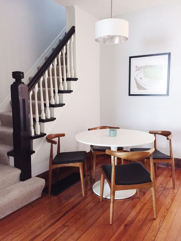 Minimalist dining area with round white table and wooden chairs beside carpeted stairs.