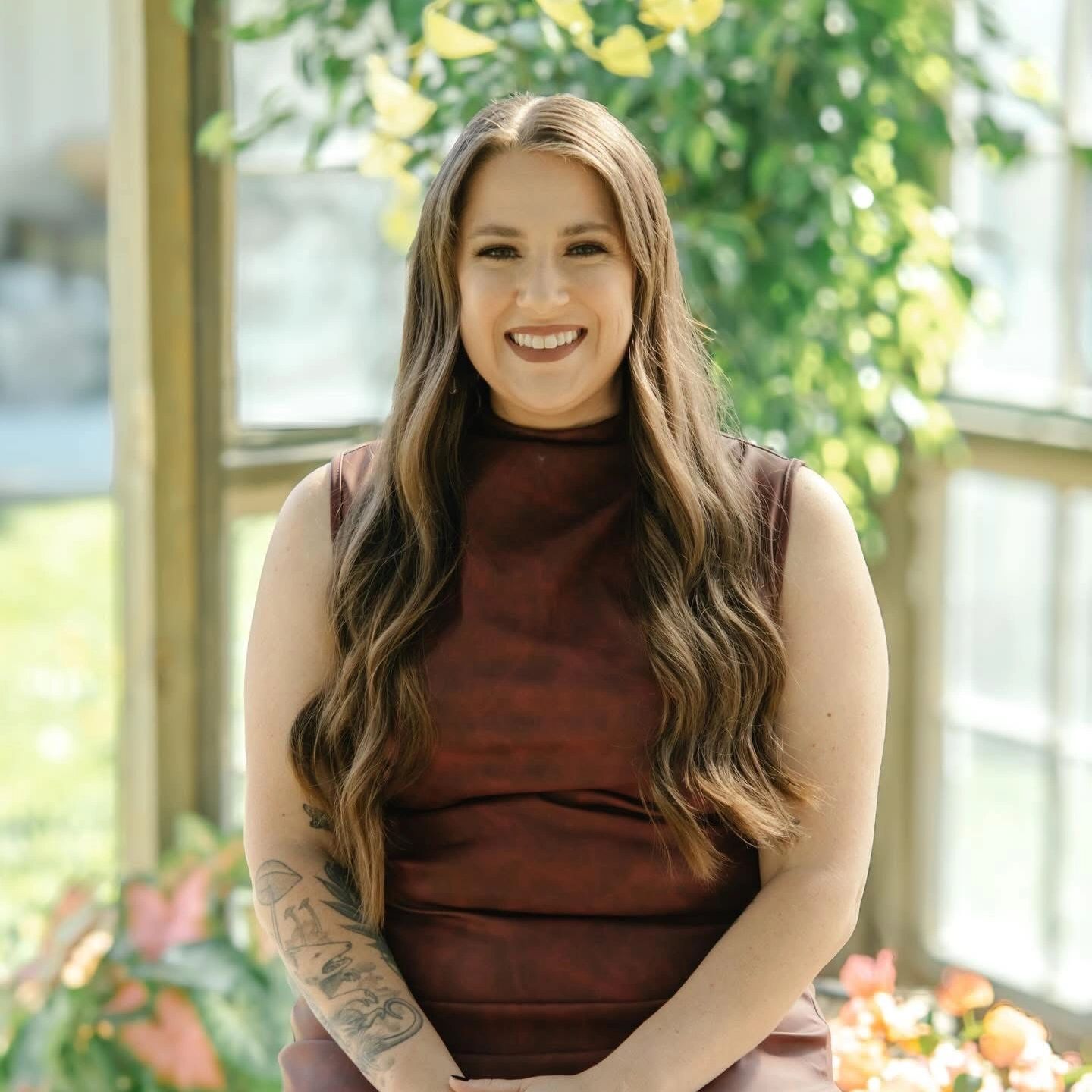 Smiling woman with long hair and tattoos in a sunlit room.