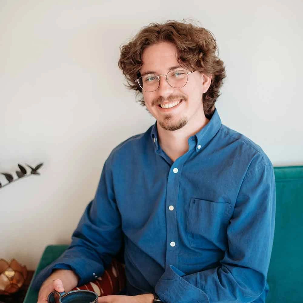 Smiling man with curly hair and glasses holding a cup.