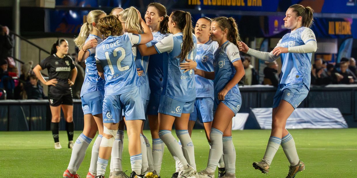 Female soccer players in blue celebrate on the field after a goal.