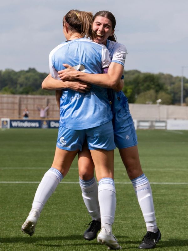 Two female soccer players joyfully embrace on the field during a game.