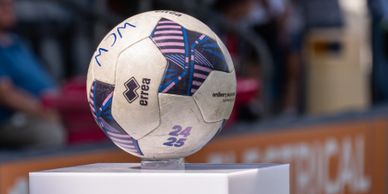A close-up of a white and blue Errea soccer ball on a pedestal.