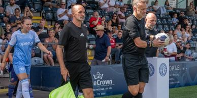 Officials and a female soccer player entering the field before a match.