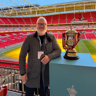Man posing with a trophy inside a large stadium with red seats.