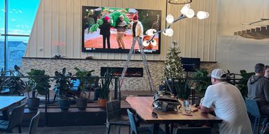 A cozy cafe with plants, a TV, and people enjoying their time.
