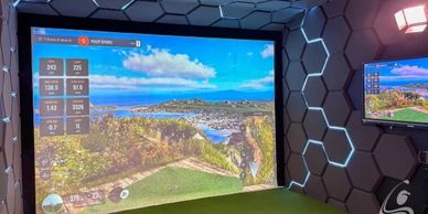 Indoor golf simulator room with hexagonal wall panels and large screen.