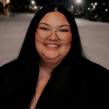 Smiling woman with long black hair and glasses at night.