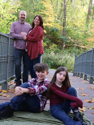 Family portrait on a wooden bridge surrounded by autumn foliage.