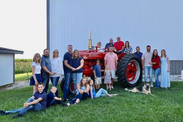 A large group poses with a vintage red tractor on a sunny day.