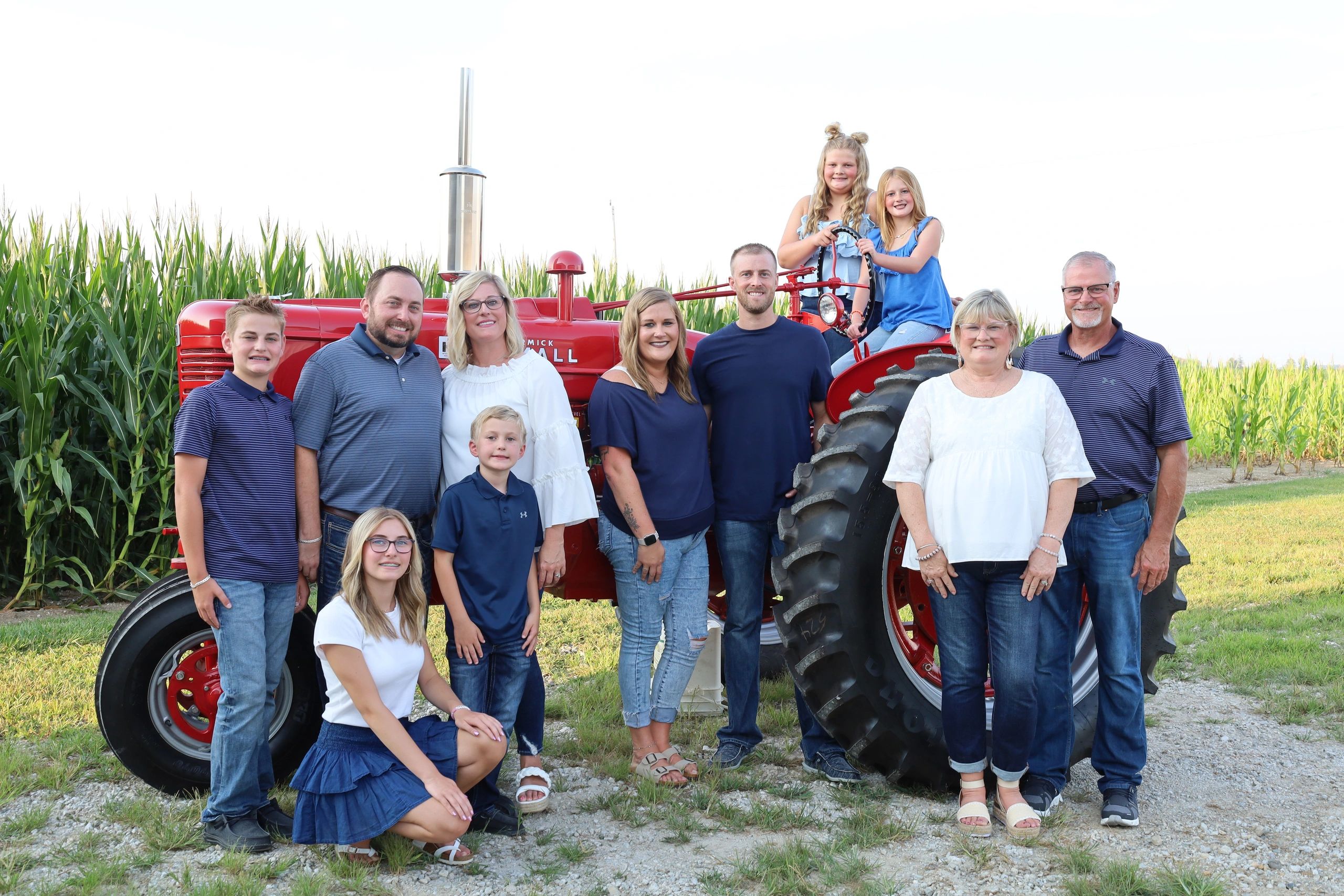Multi-generational family posing with a red tractor in a cornfield.