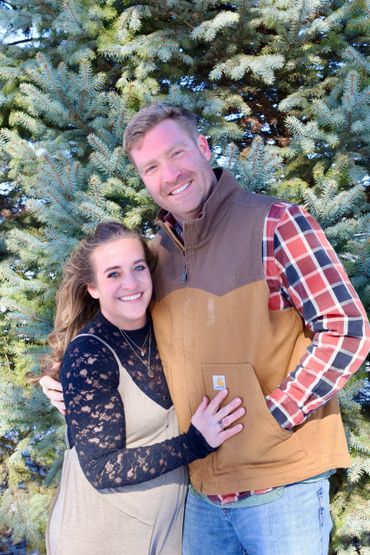 Happy couple posing outdoors in front of a pine tree.