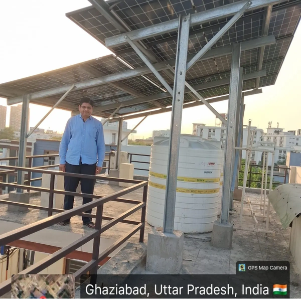 Man standing on rooftop with solar panels and water tank.