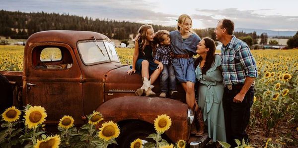 Family enjoying time together on an old truck in a sunflower field.