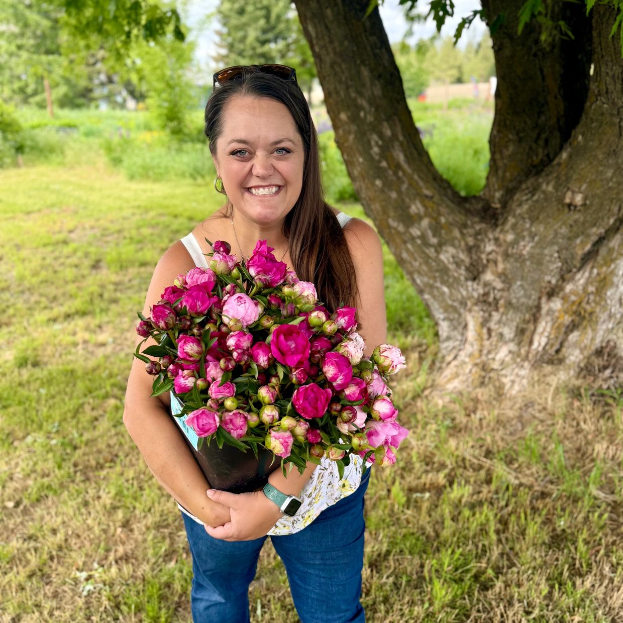 Smiling woman holding a large bouquet of vibrant pink flowers outdoors.