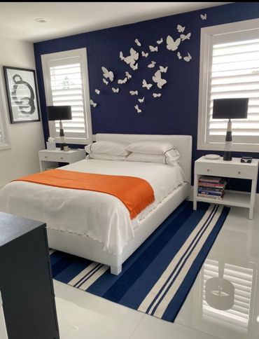 Navy blue Accent wall with white butterfly’s, white bedding with orange throw