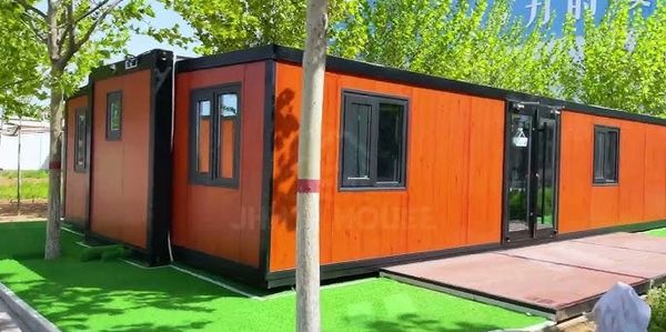 Modern orange modular building with black frames surrounded by trees.