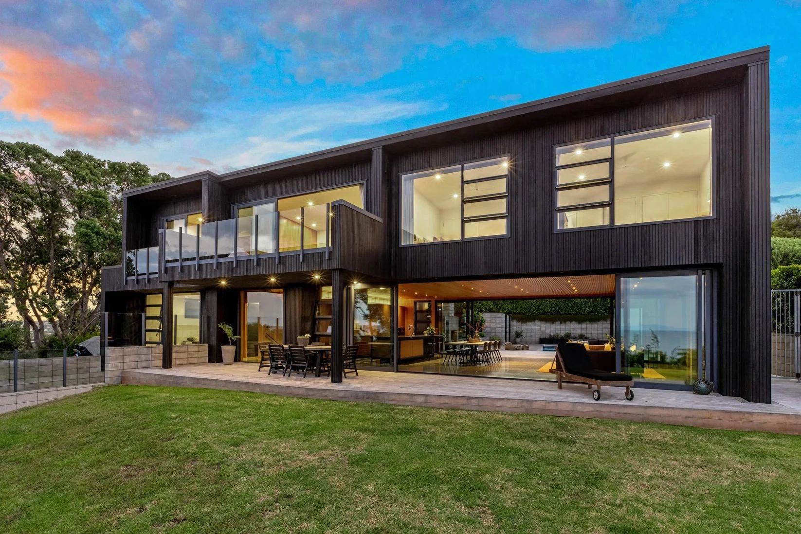 Modern two-story house with large windows and outdoor seating.