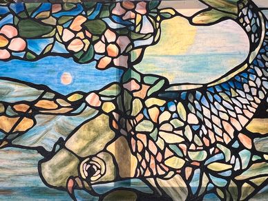 A stained glass painting of a fish on muslin, with light shining through.