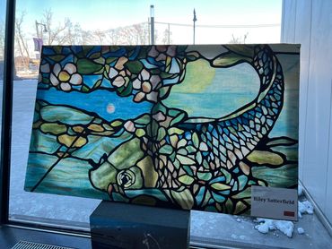 Stained glass painting of a fish leaned up against a window, catching natural light through it.