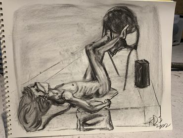 Figure drawing study done in charcoal. 
A nude figure lies on the ground with their legs on a chair.