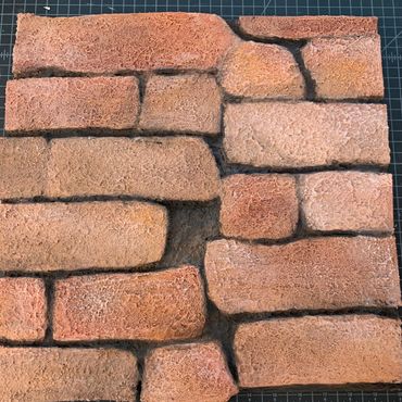 Small masonite sheet filled with foam rectangles carved and painted to be brick texture.